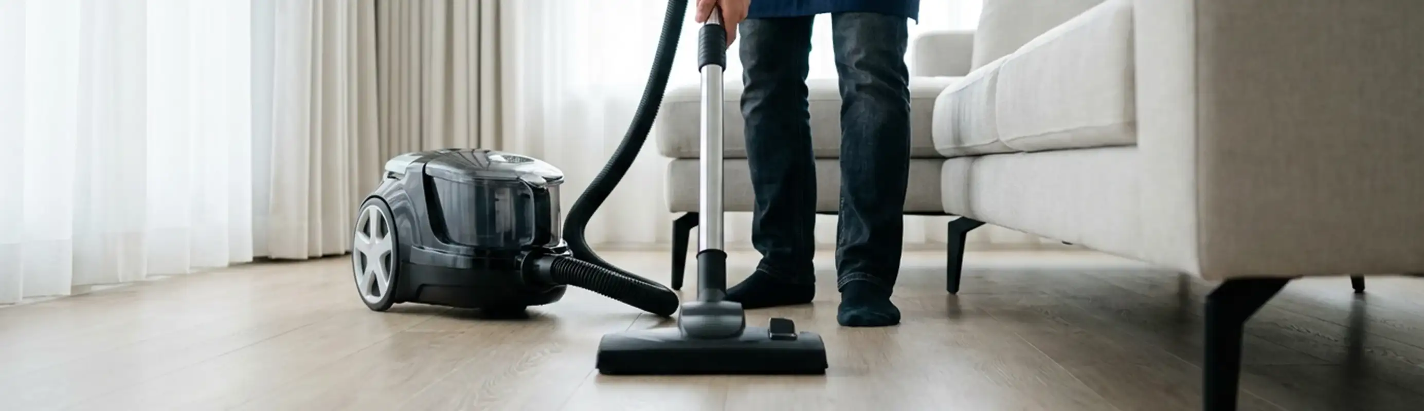 Professional house cleaner vacuuming a living room floor with a canister vacuum cleaner, Cape Coral, FL.