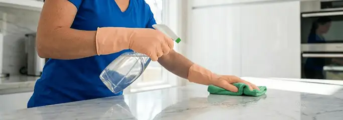 Maid service worker spraying and wiping a kitchen countertop with a microfiber cloth for sanitizing, Cape Coral, FL.
