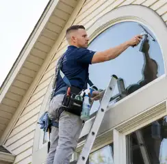Professional window cleaner on a ladder using a squeegee to clean an exterior arched window, Cape Coral, FL.