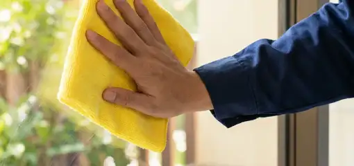 House cleaner wiping a glass window with a yellow microfiber cloth for streak-free cleaning, Cape Coral, FL.